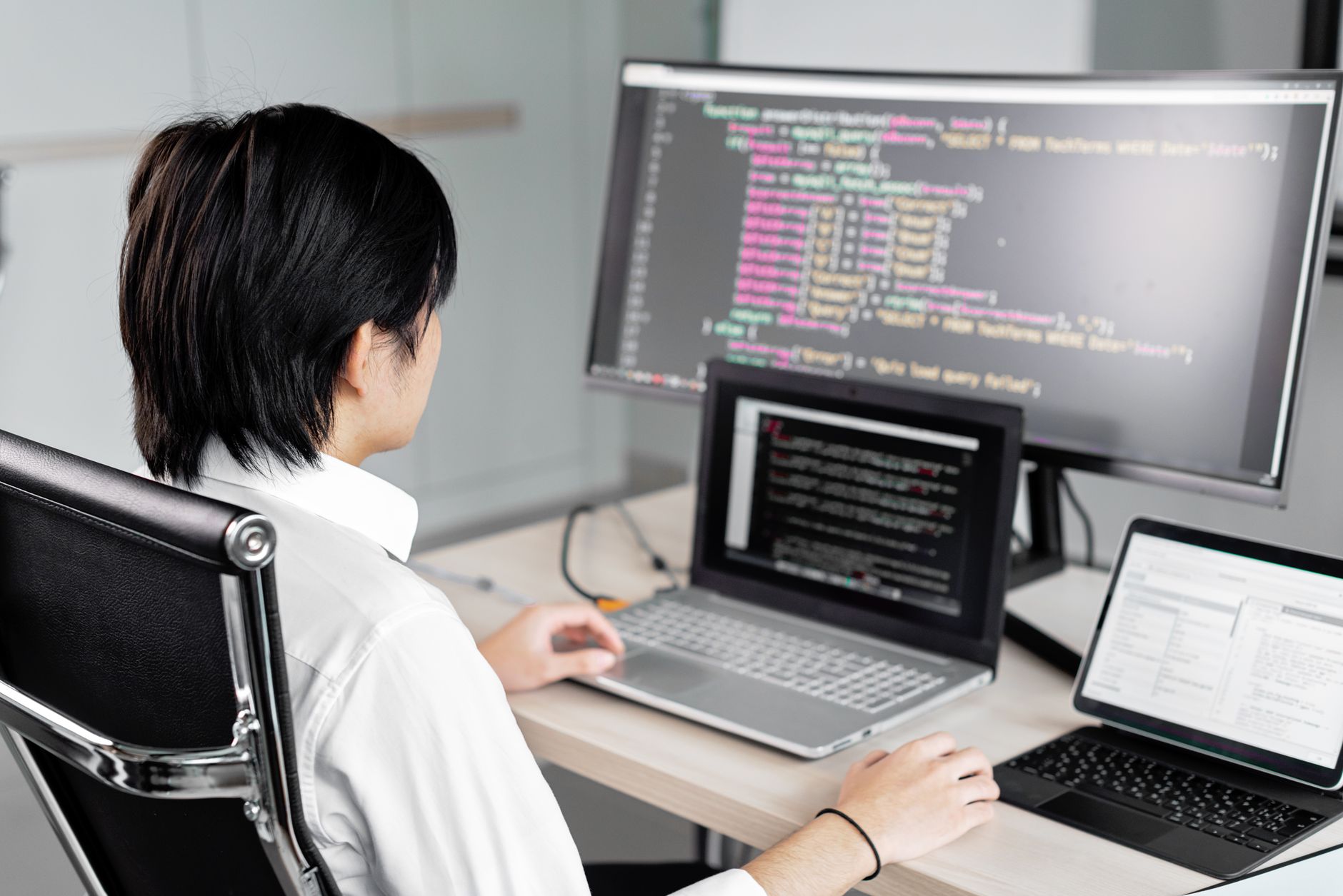 Une personne assise à un bureau travaille devant un grand écran affichant des lignes de code informatique.
